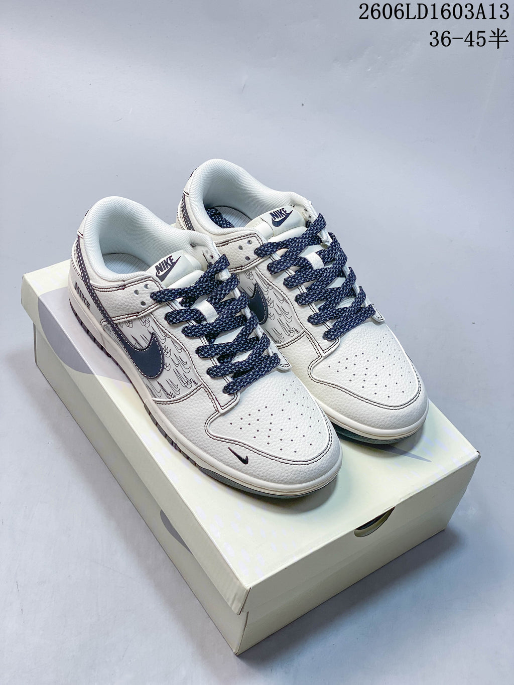 Pair of cream and navy low-top Nike Dunk sneakers with patterned side panels, displayed on a box.