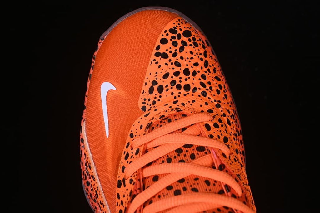 Top-down view of the orange toe panel, laces, and spotted upper.