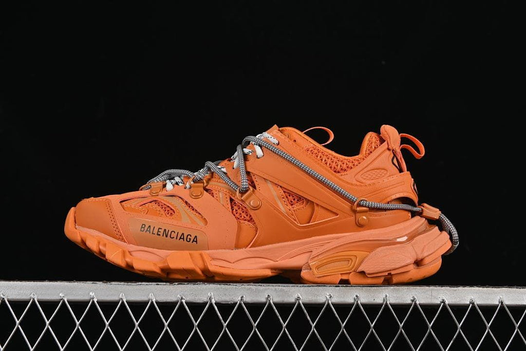 Side view of orange Balenciaga Track sneakers against a dark background