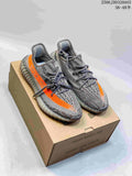 Pair of gray Adidas Yeezy Boost 350 V2 sneakers with orange side stripes on a shoe box; image overlay states 36–48.5.