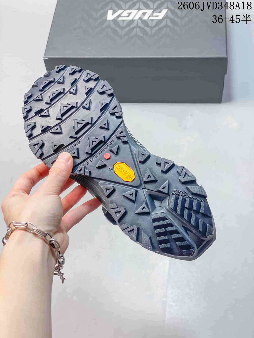 Close-up of the trail shoes' lugged outsole, with the shoebox in the background.