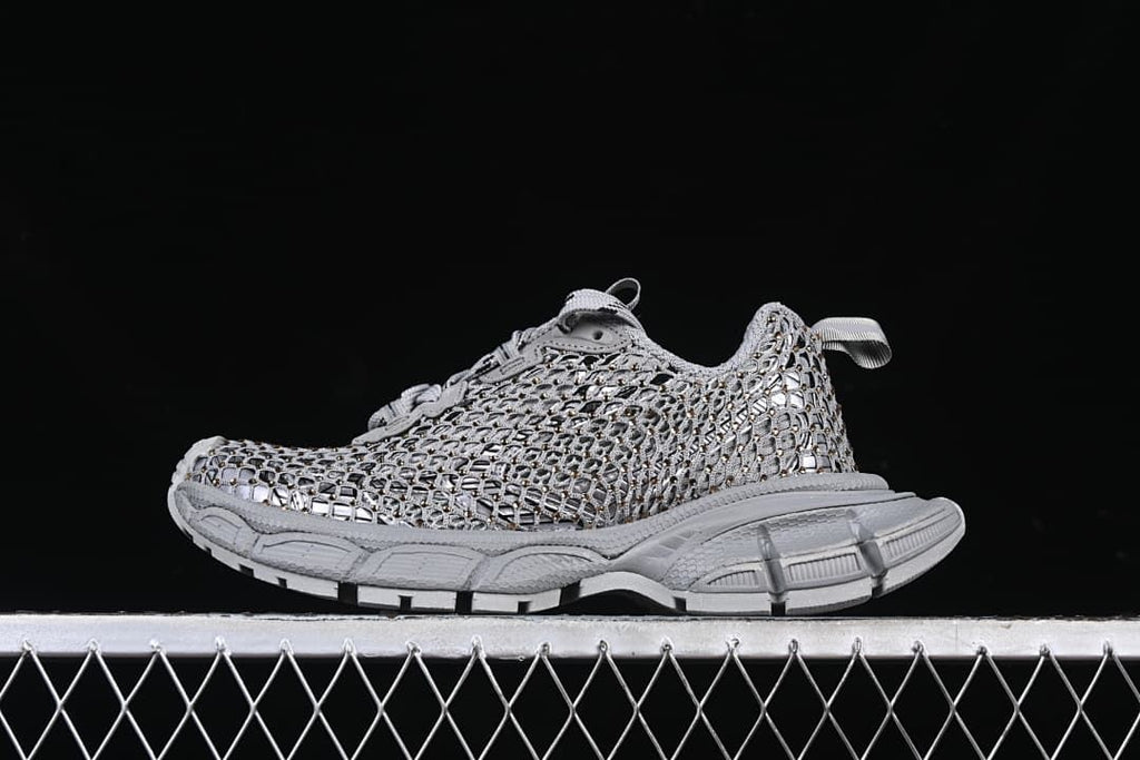 Side view of the grey sneaker with openwork upper and gold-tone accents.