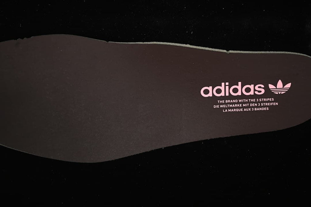 Dark shoe insert with adidas branding and pink trefoil logo.