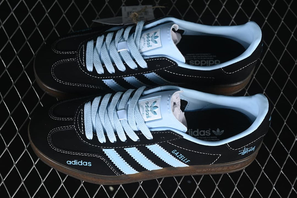 Pair of black Gazelle Indoor sneakers with light blue stripes and gum soles