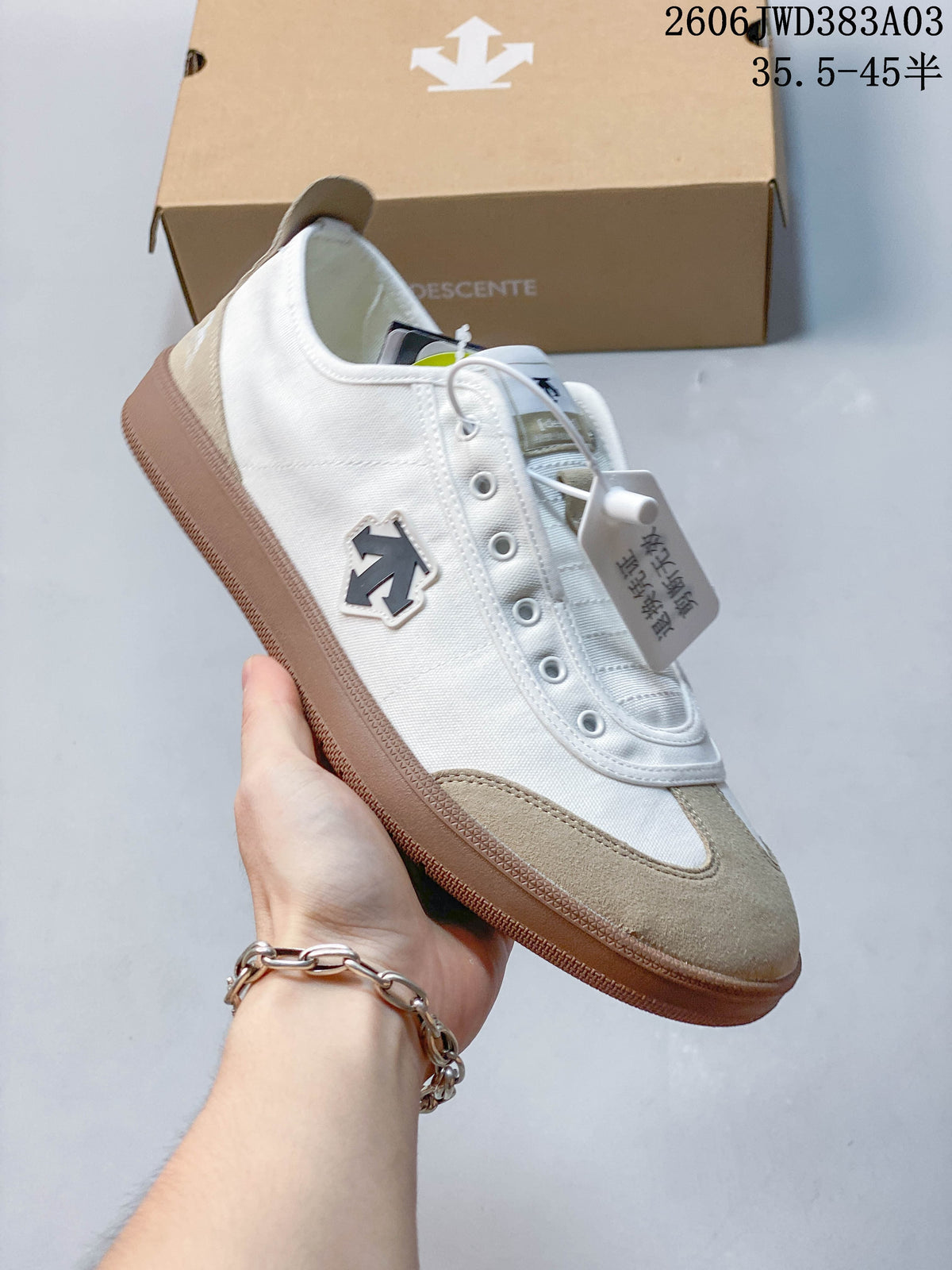 Side view of the white sneaker with beige overlays and DESCENTE side emblem
