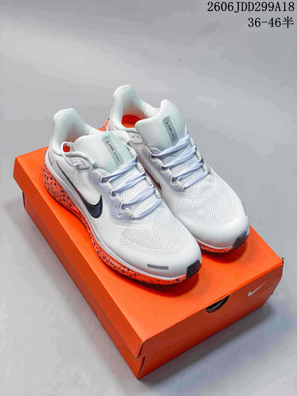 White Nike running shoes with orange and dark speckled sole accents on an orange shoe box