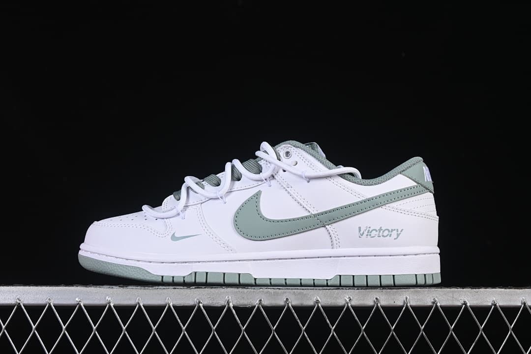 Side view of a white and sage-green Nike SB Dunk Low sneaker with Victory lettering on the heel.