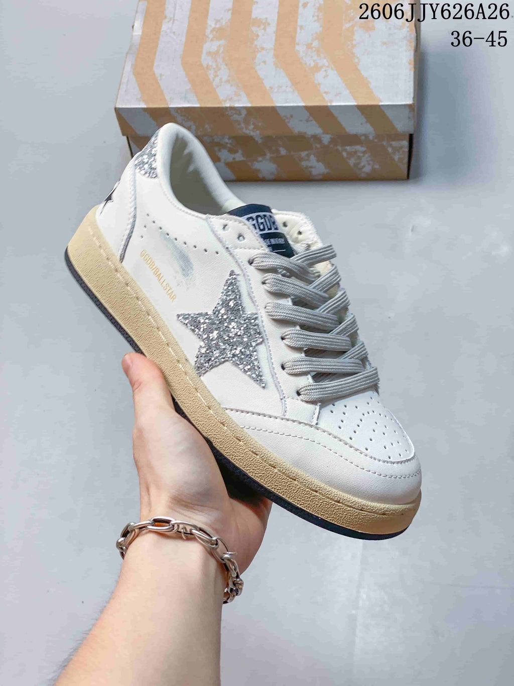 White low-top sneaker with a silver glitter-style star, gray laces, perforated toe, and distressed-look beige sole.