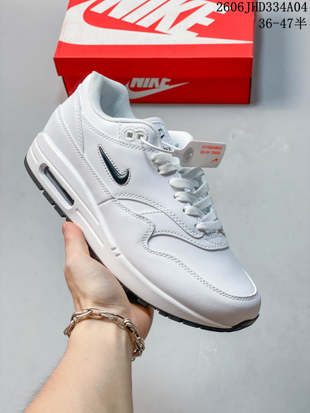 White Nike Air Max 1 sneaker with dark overlays and a visible Air unit in the midsole.
