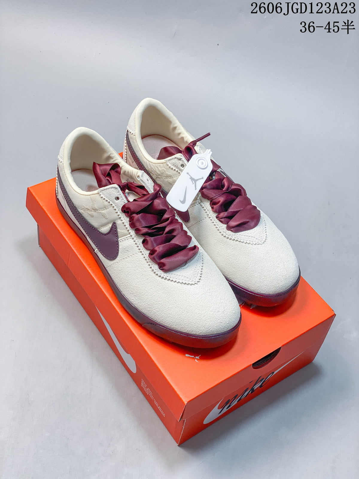 Pair of off-white Nike Astro Grabber low-top sneakers with plum accents and wide laces, shown on an orange shoe box