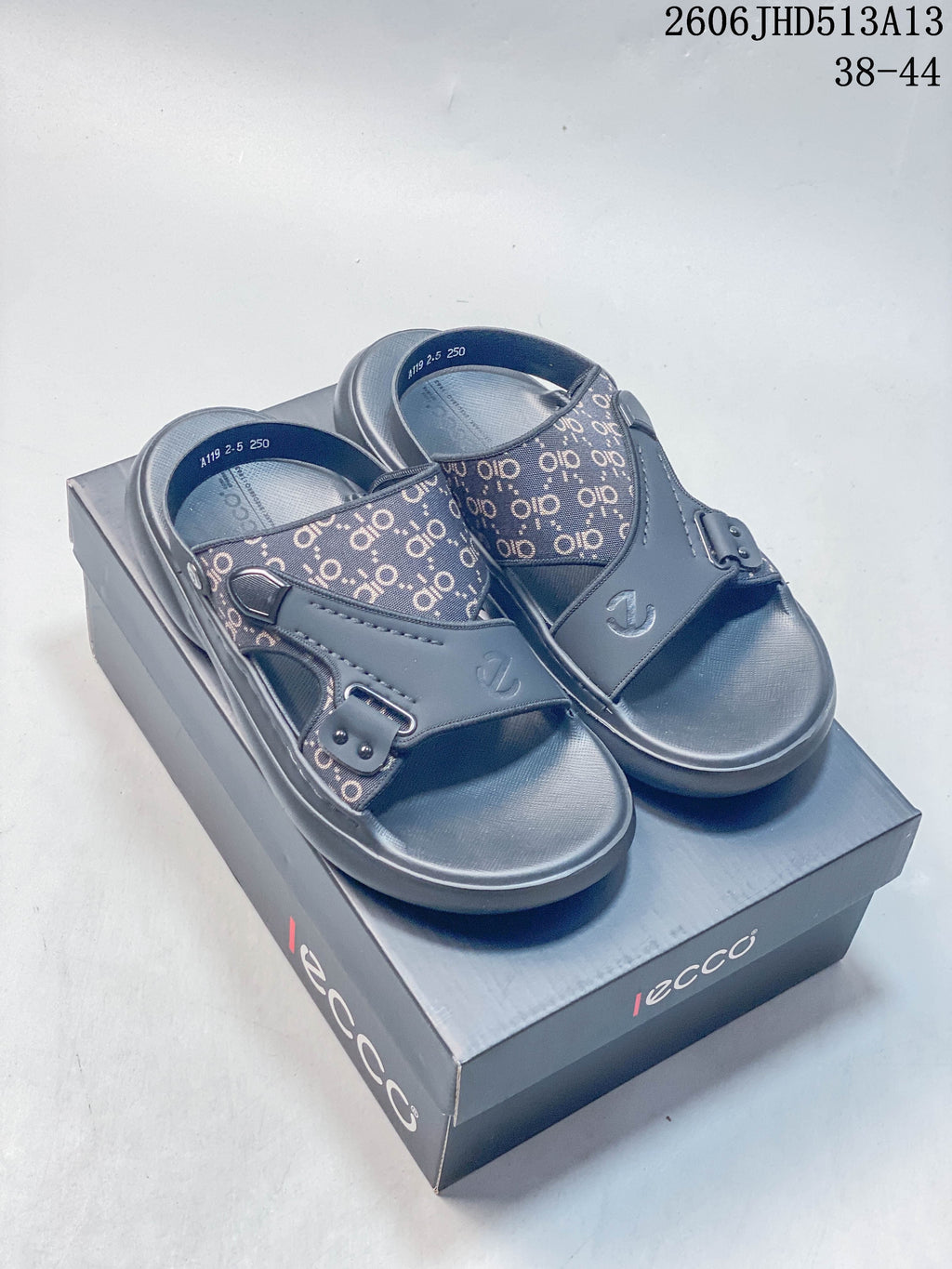 Pair of gray open-toe slide sandals with patterned panels, shown on a branded box.