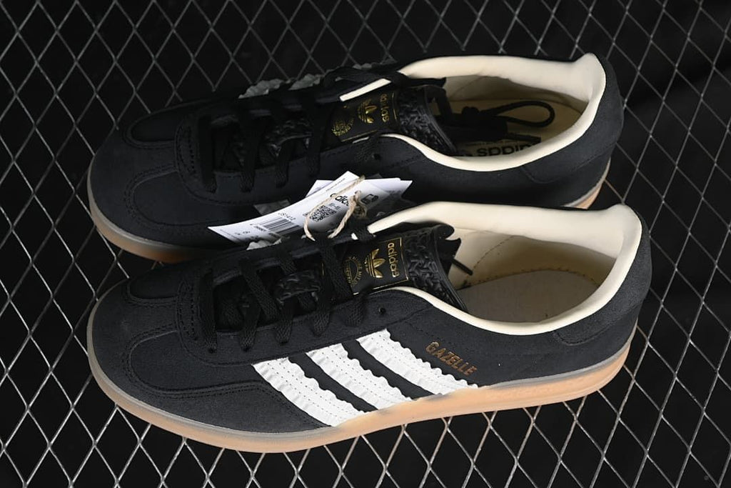 Pair of black Adidas Gazelle Indoor sneakers with white stripes and gum-colored soles.
