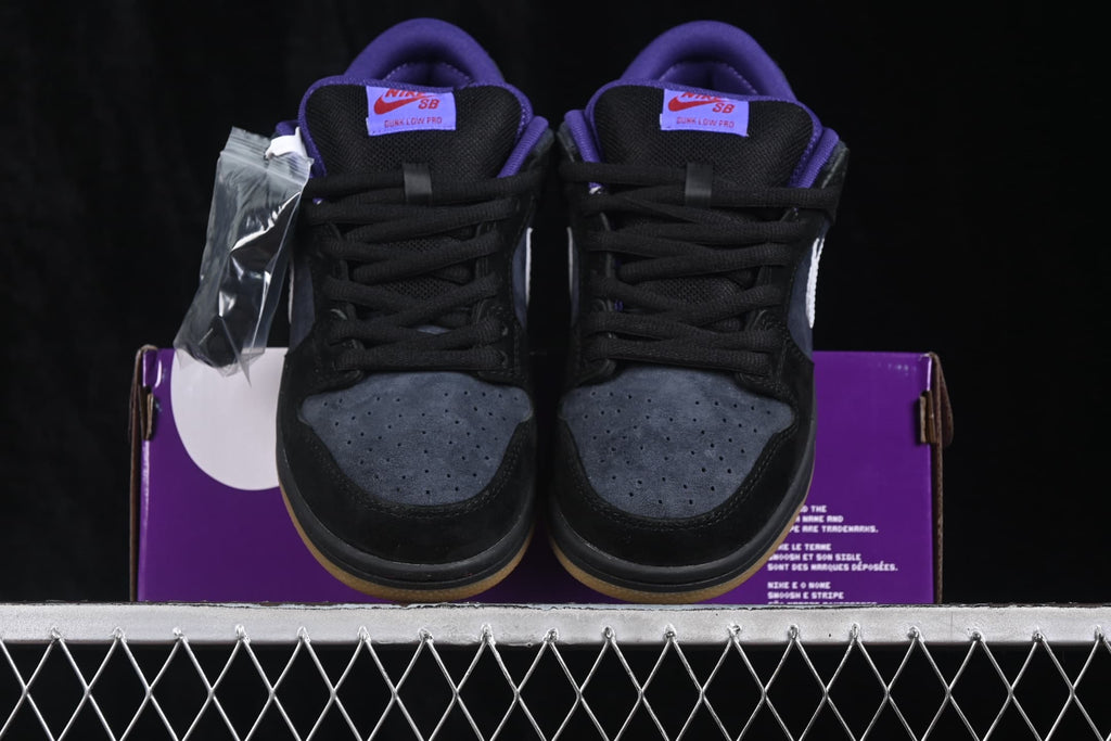 Pair of Nike SB Dunk Low sneakers shown from the front in black, navy, purple, and gum tones.