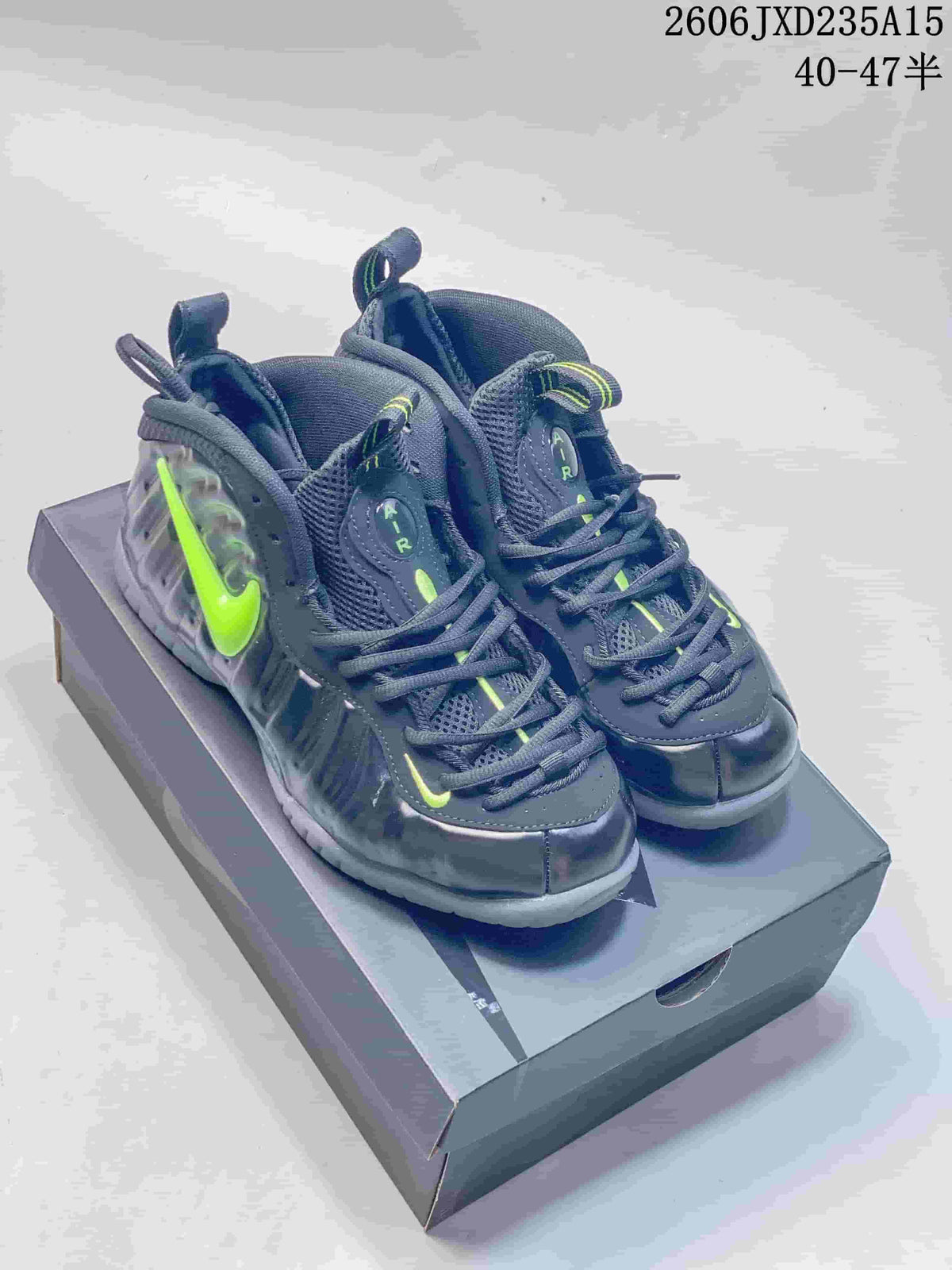 Pair of dark gray and black Nike Foamposite One shoes with volt-green accents, shown from the front at an angle.