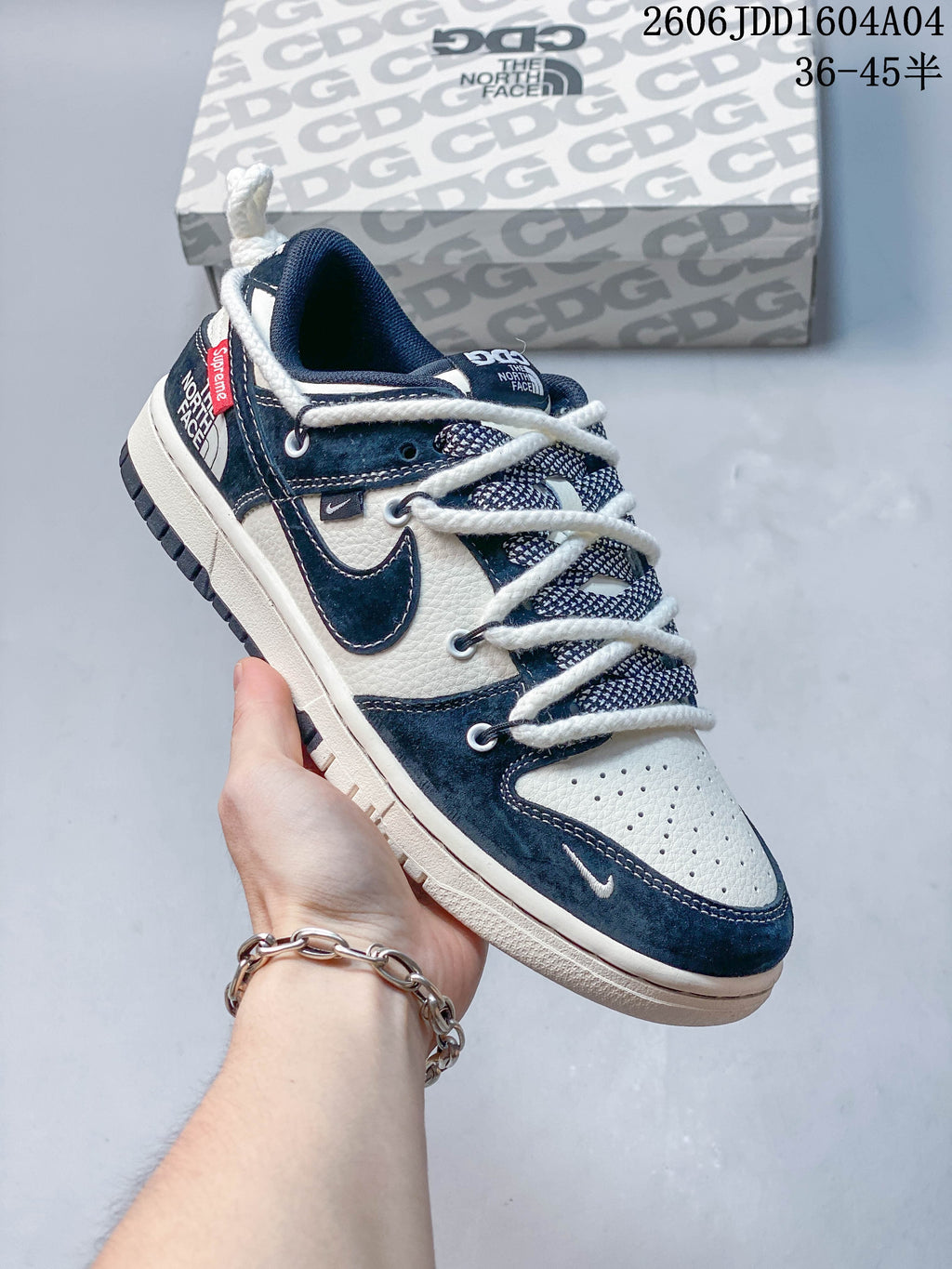 Navy and cream low-top sneaker with contrasting overlays and thick white laces, shown beside a patterned box.