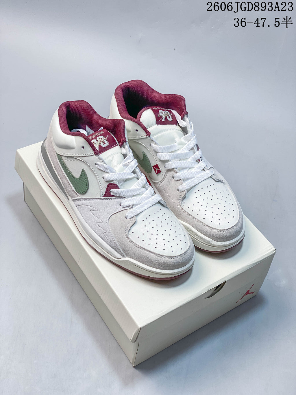 Pair of Jordan Stadium 90 sneakers in white, pale grey, green and burgundy, shown on a box