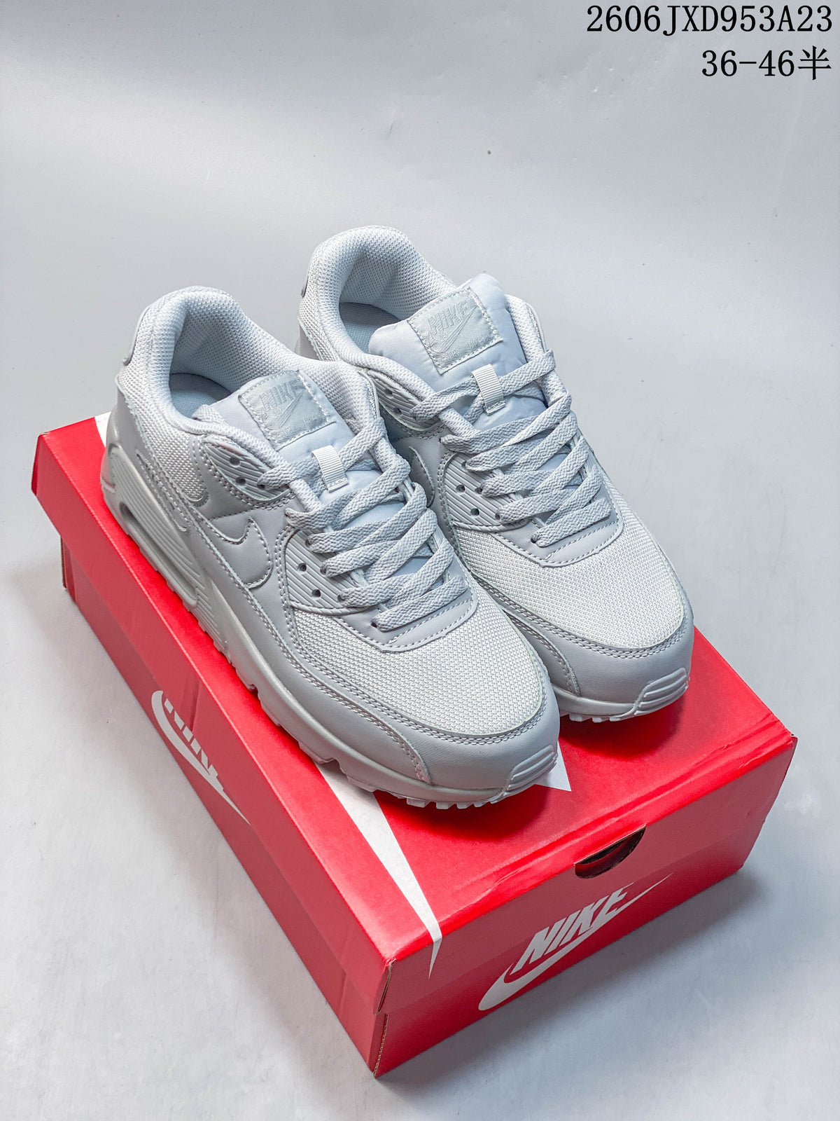 Pair of light grey Nike Air Max 90 low-top sneakers displayed on a red shoe box