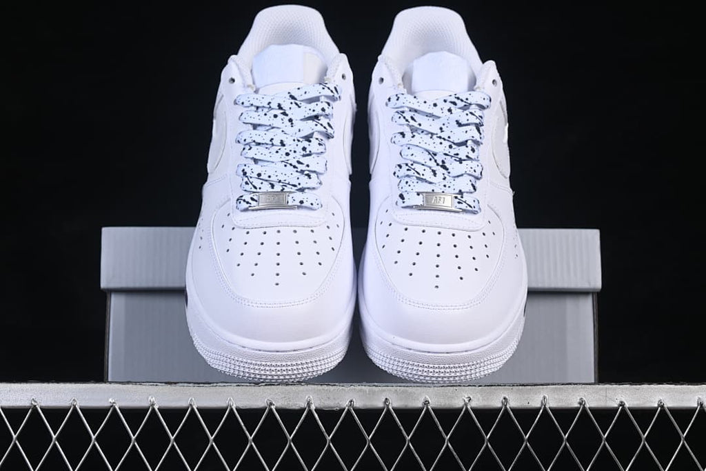 Front view of white low-top sneakers with black-speckled laces and perforated toe panels