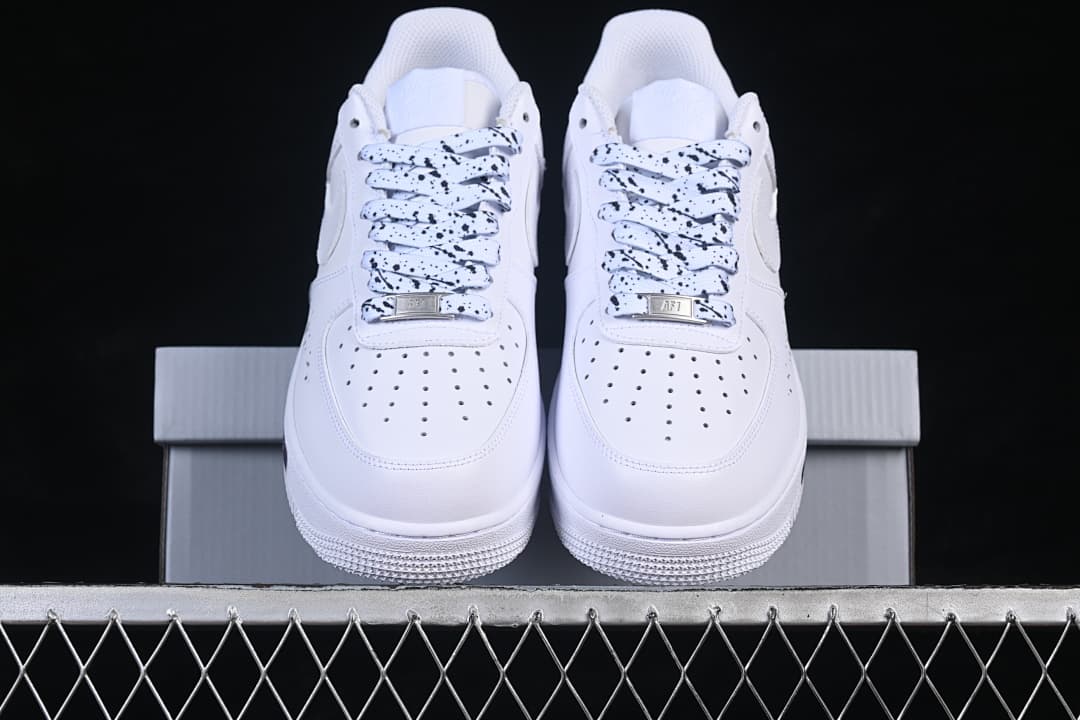 Front view of white low-top sneakers with black-speckled laces and perforated toe panels