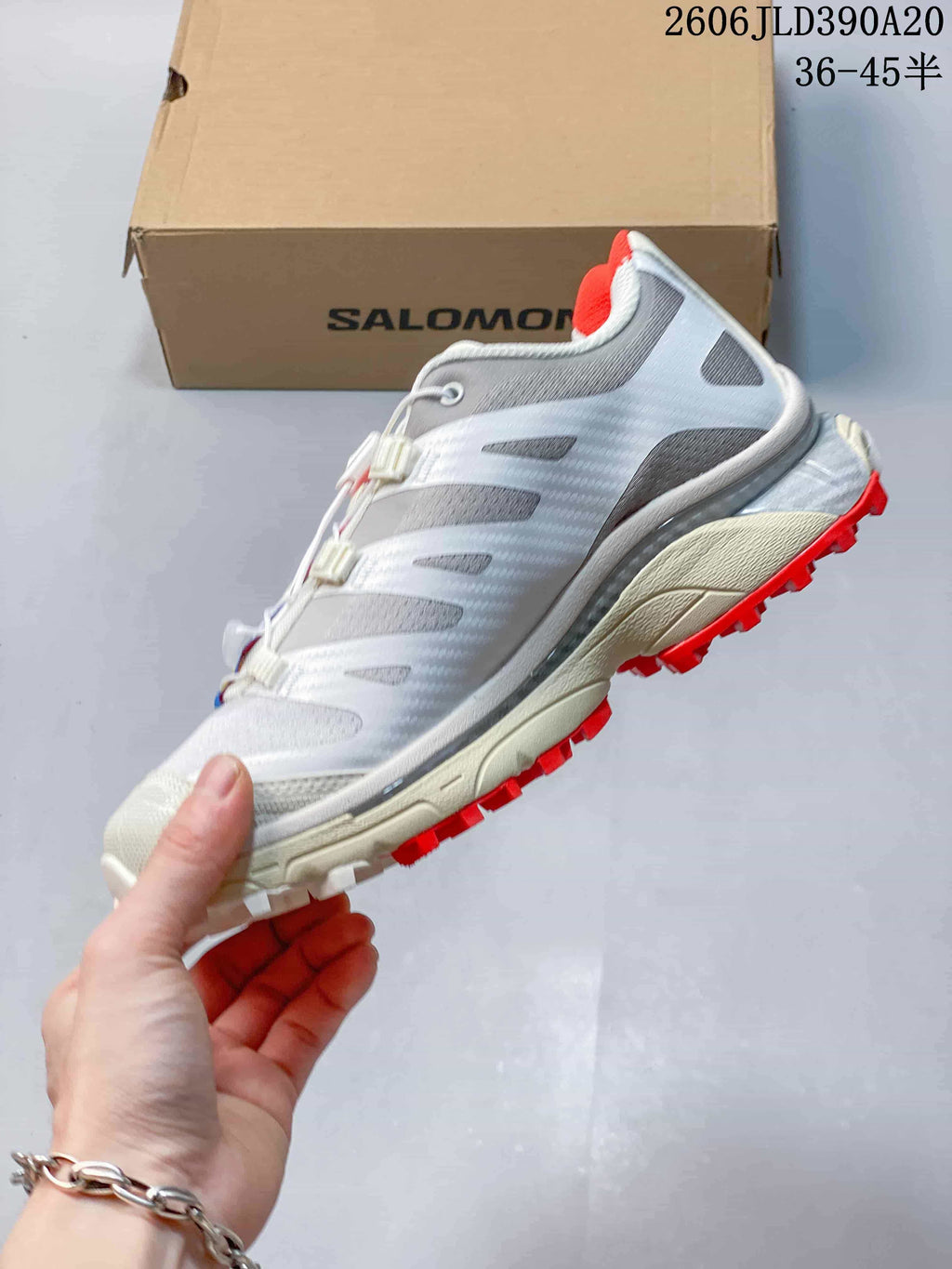 Side view of the white and gray trail shoe with red outsole lugs.