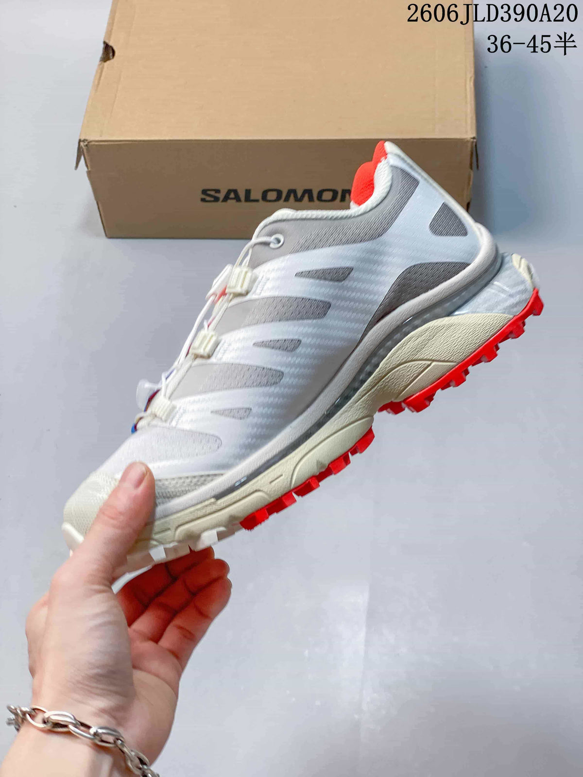 Side view of the white and gray trail shoe with red outsole lugs.