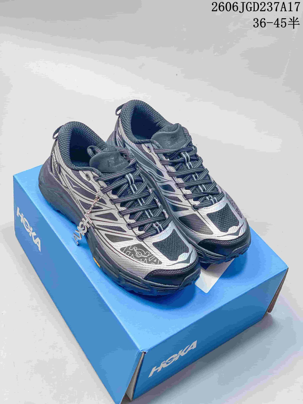 Pair of silver-grey and charcoal HOKA U Mafate Speed 2 trail shoes on a blue box