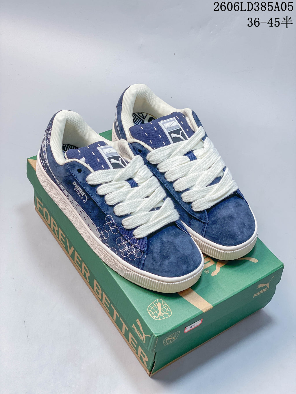 Pair of blue PUMA Suede XL sneakers with white laces and patterned side panels, shown on a green shoebox.