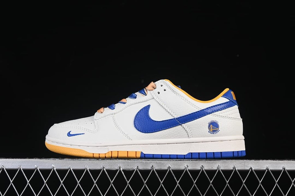 Side view of a white Nike SB Dunk Low with blue and gold-toned accents and Golden State Warriors heel branding.