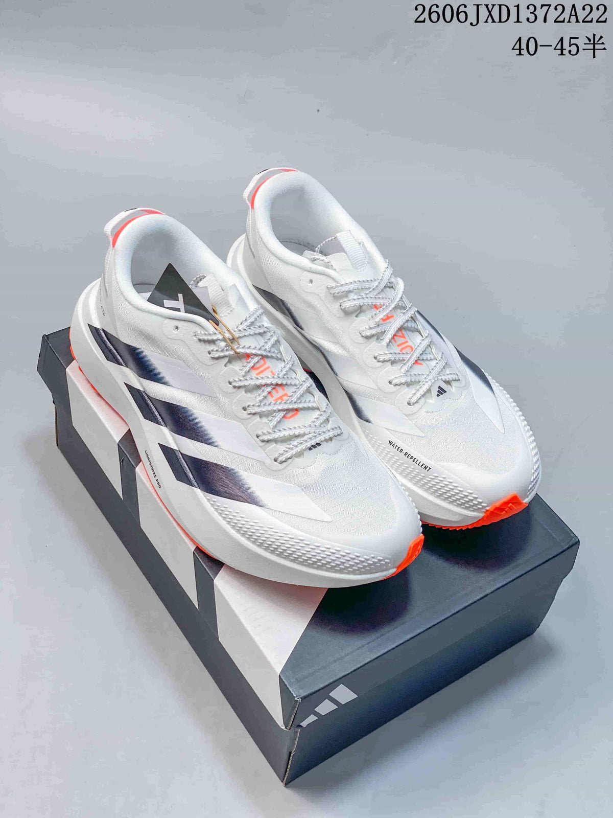 Pair of white Adidas Adizero Evo SL ATR shoes with dark side stripes and orange outsole accents, shown on a shoe box.