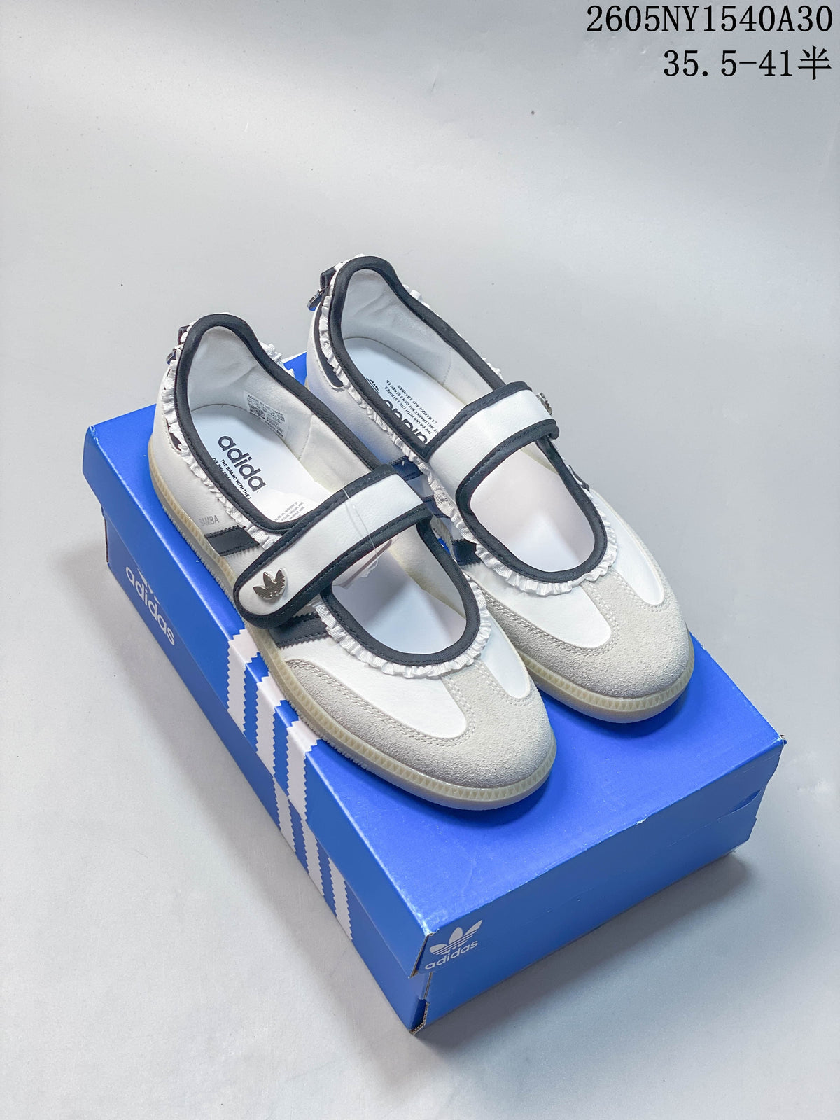 White and black Adidas Samba Jane Mary Jane sneakers shown on a blue box