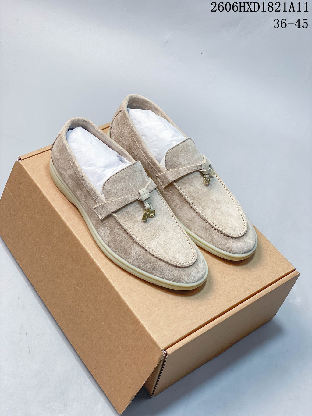 Pair of beige suede-style Loro Piana lock-detail loafers shown from above on a box.