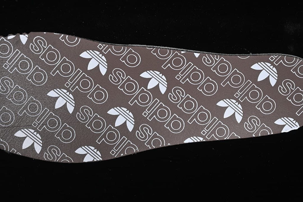 Brown shoe insole with repeating adidas branding and trefoil motifs
