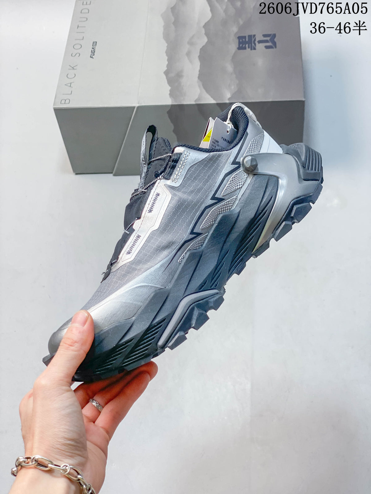 Side view of the silver-gray trail shoe with a dark lugged sole and external heel support.