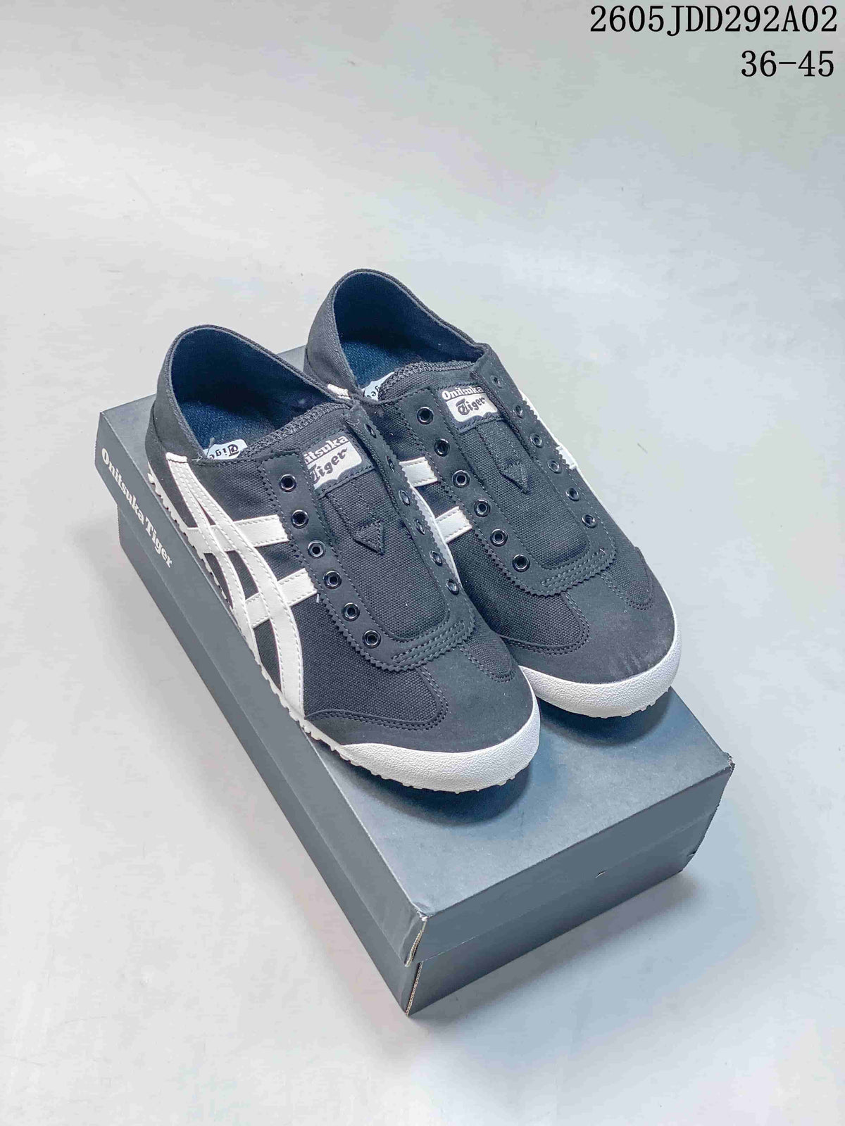 Pair of charcoal Onitsuka Tiger slip-on sneakers with white side stripes, shown on a branded box