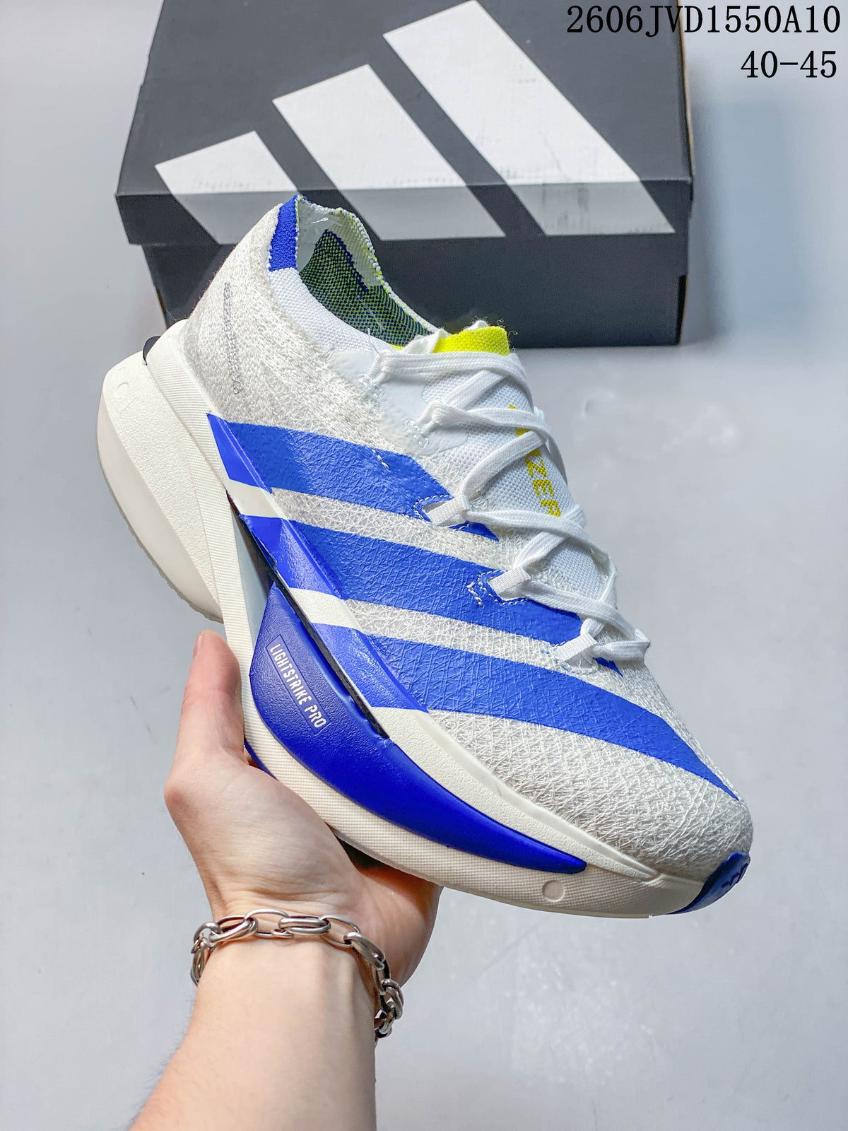 Side view of a white Adidas Adizero Prime X3 running shoe with blue stripes and yellow accents.
