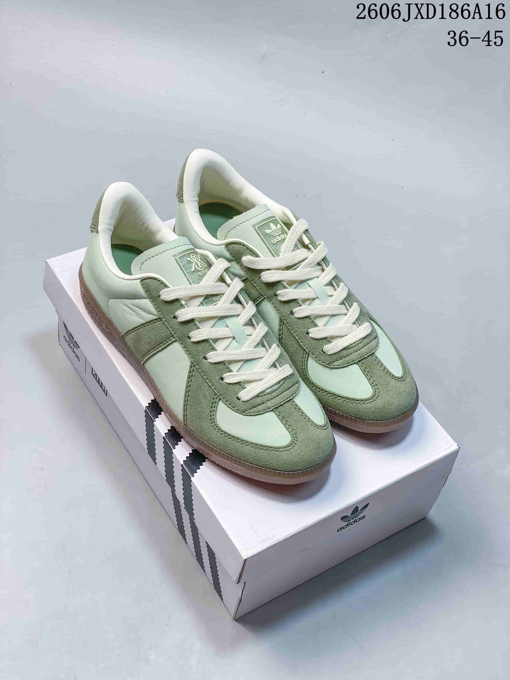 Pair of pale green Kith x adidas BW Army low-top sneakers with cream laces and gum-colored soles on a shoebox.