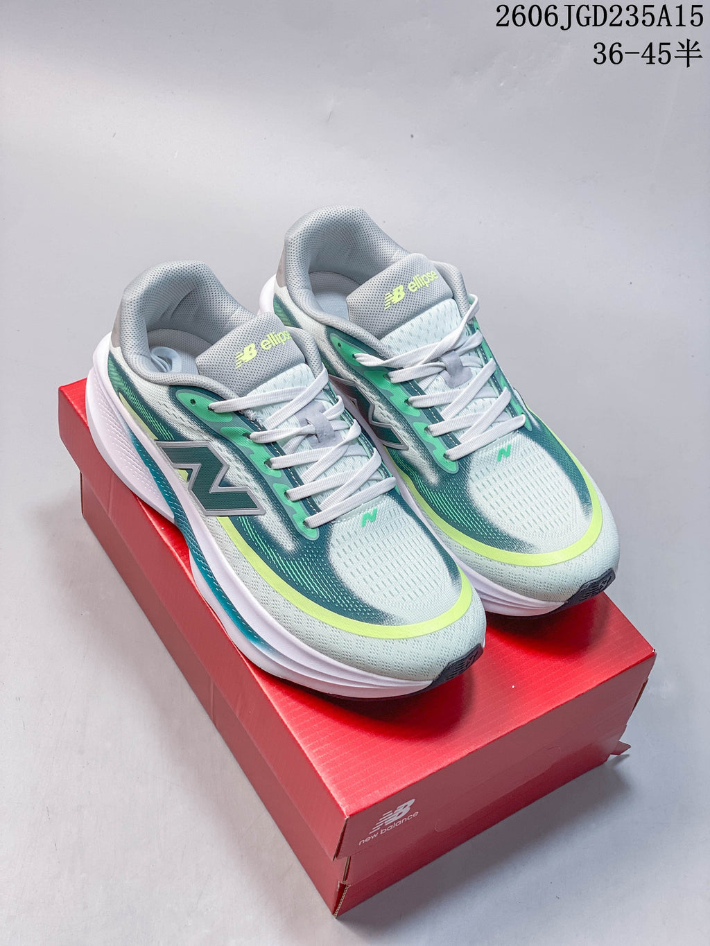 Pair of pale gray New Balance Ellipse running shoes with teal and lime accents, shown on a red shoe box.