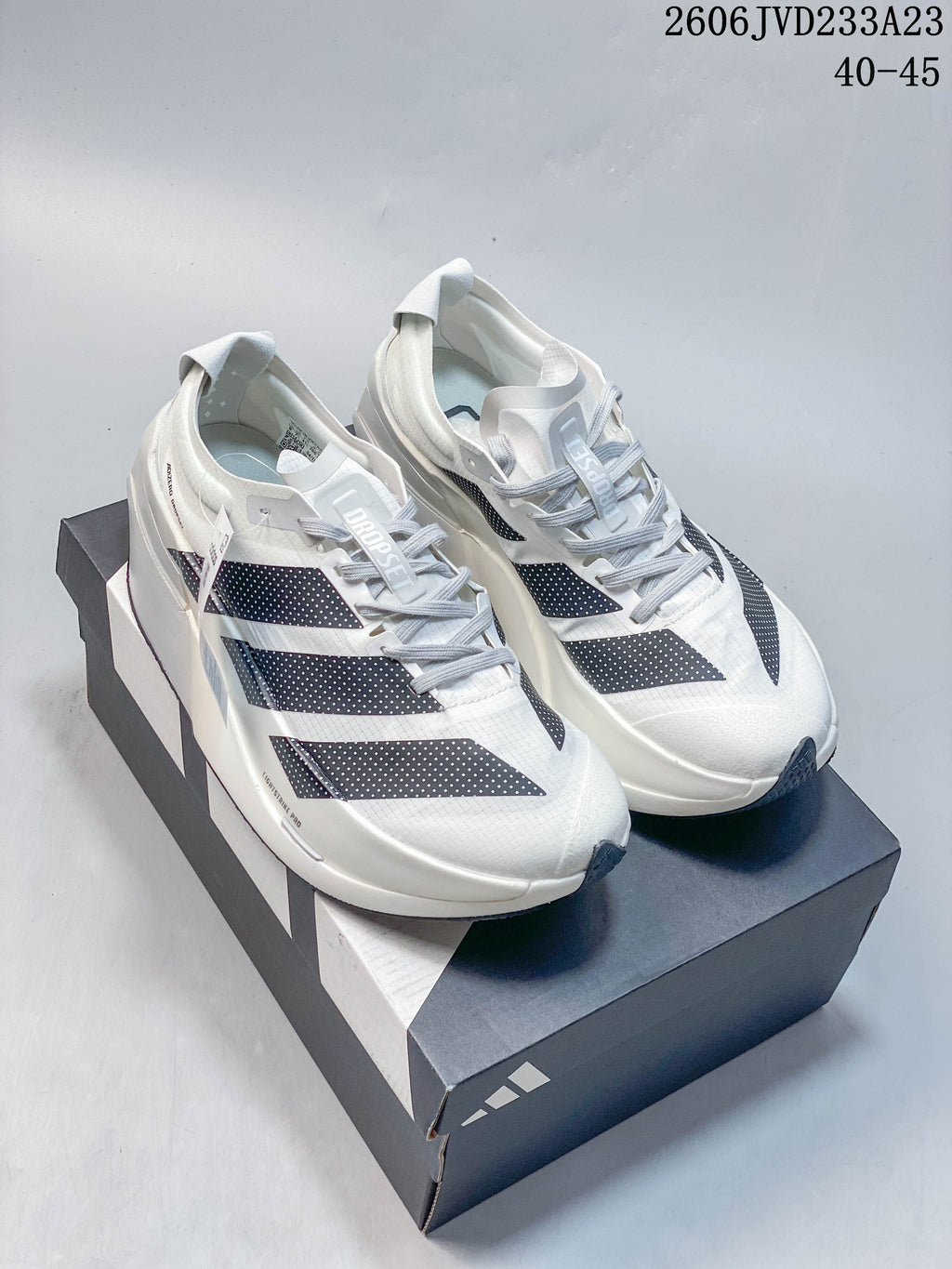 Pair of white adidas Adizero Prime X3 running shoes with dark patterned stripes, displayed on a shoe box