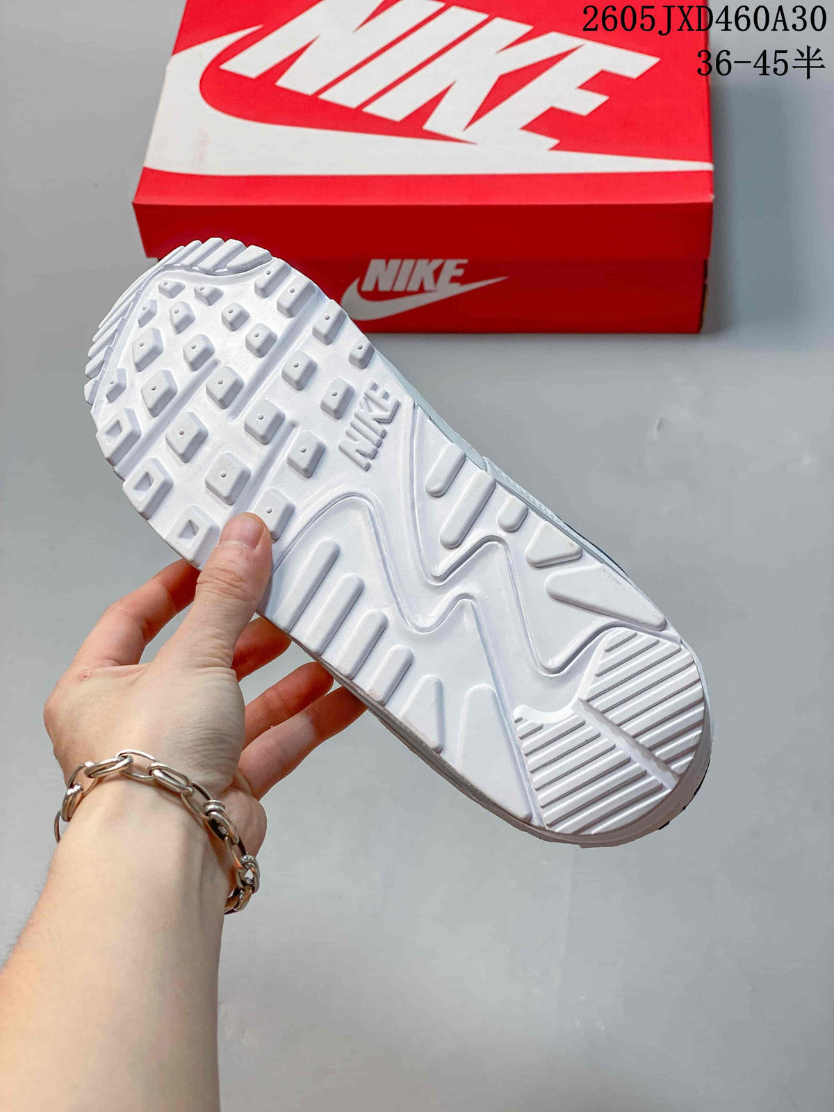 White outsole of a Nike Air Max 90 sneaker, with a red shoe box in the background