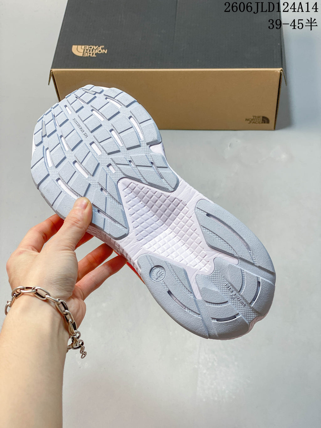 Close-up of the gray and white tread on an orange trail-running shoe