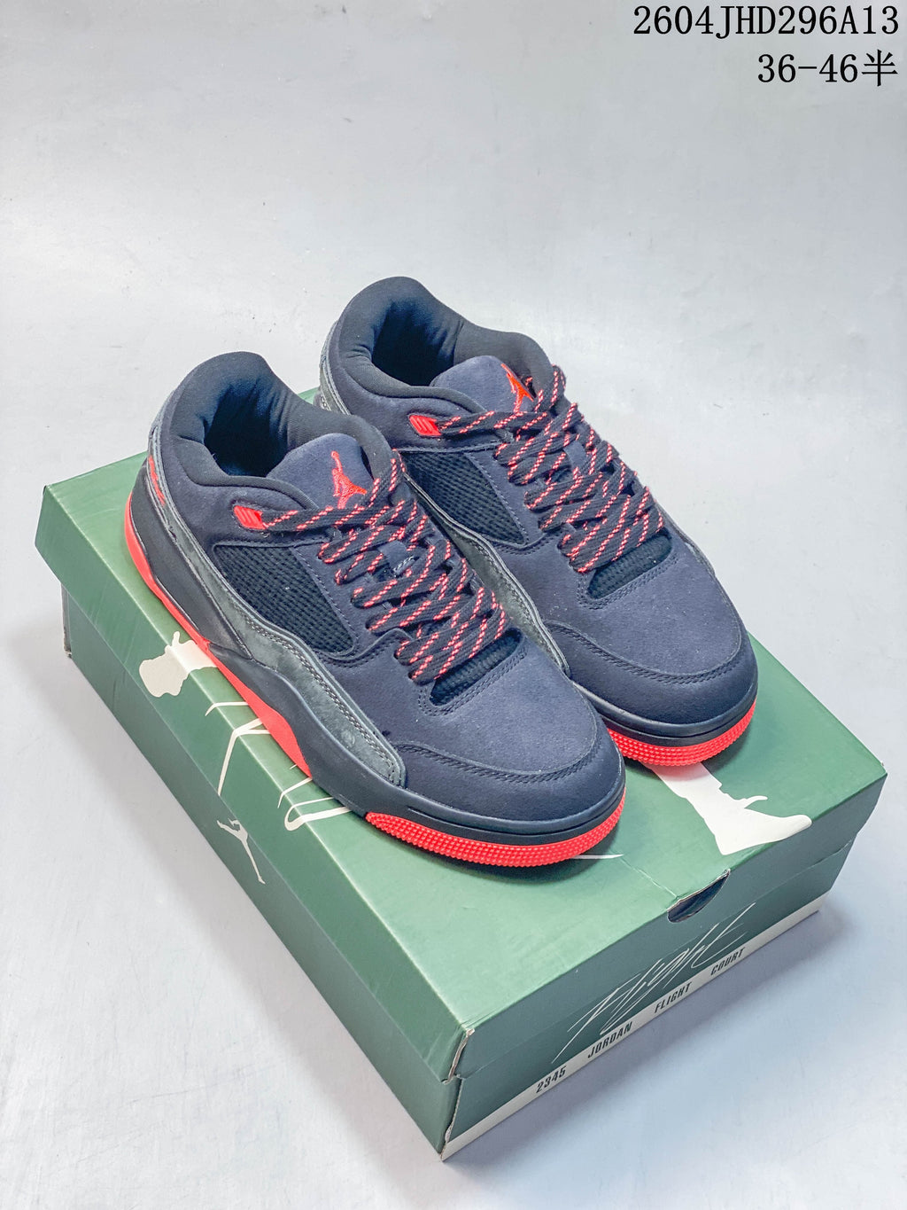 Pair of navy Jordan low-top sneakers with gray panels and red accents, shown on a green shoe box.