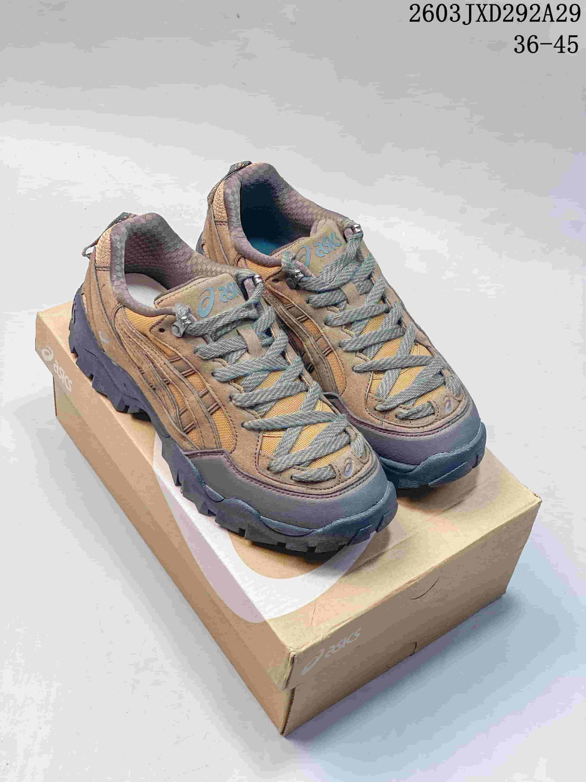 Pair of tan and brown ASICS Gel-Pickax hiking sneakers with mustard panels and dark lugged soles, shown on a shoe box.