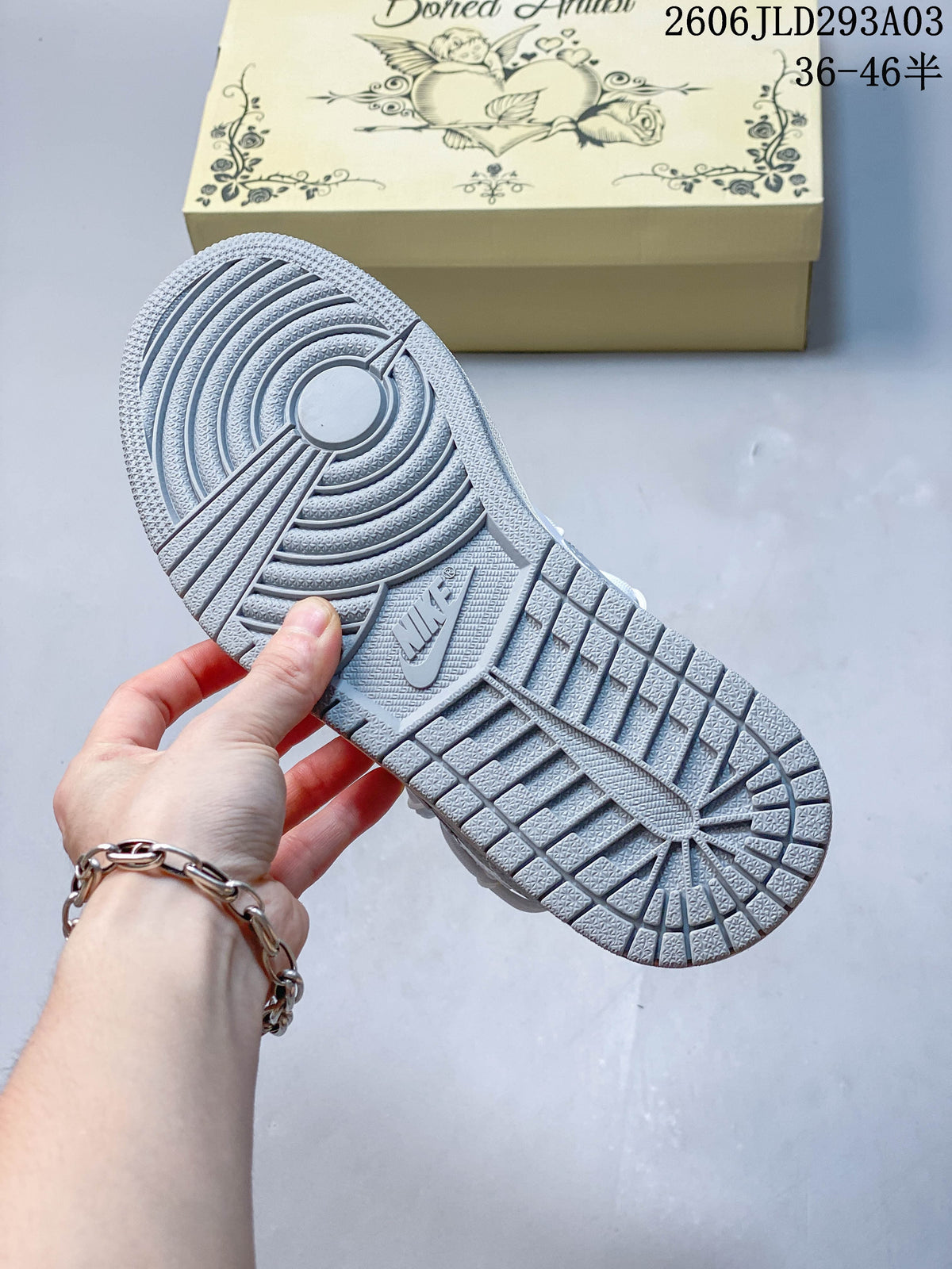 Close-up of the gray patterned outsole and patterned shoe box; overlay shows code 2606JLD293A03 and a size range.