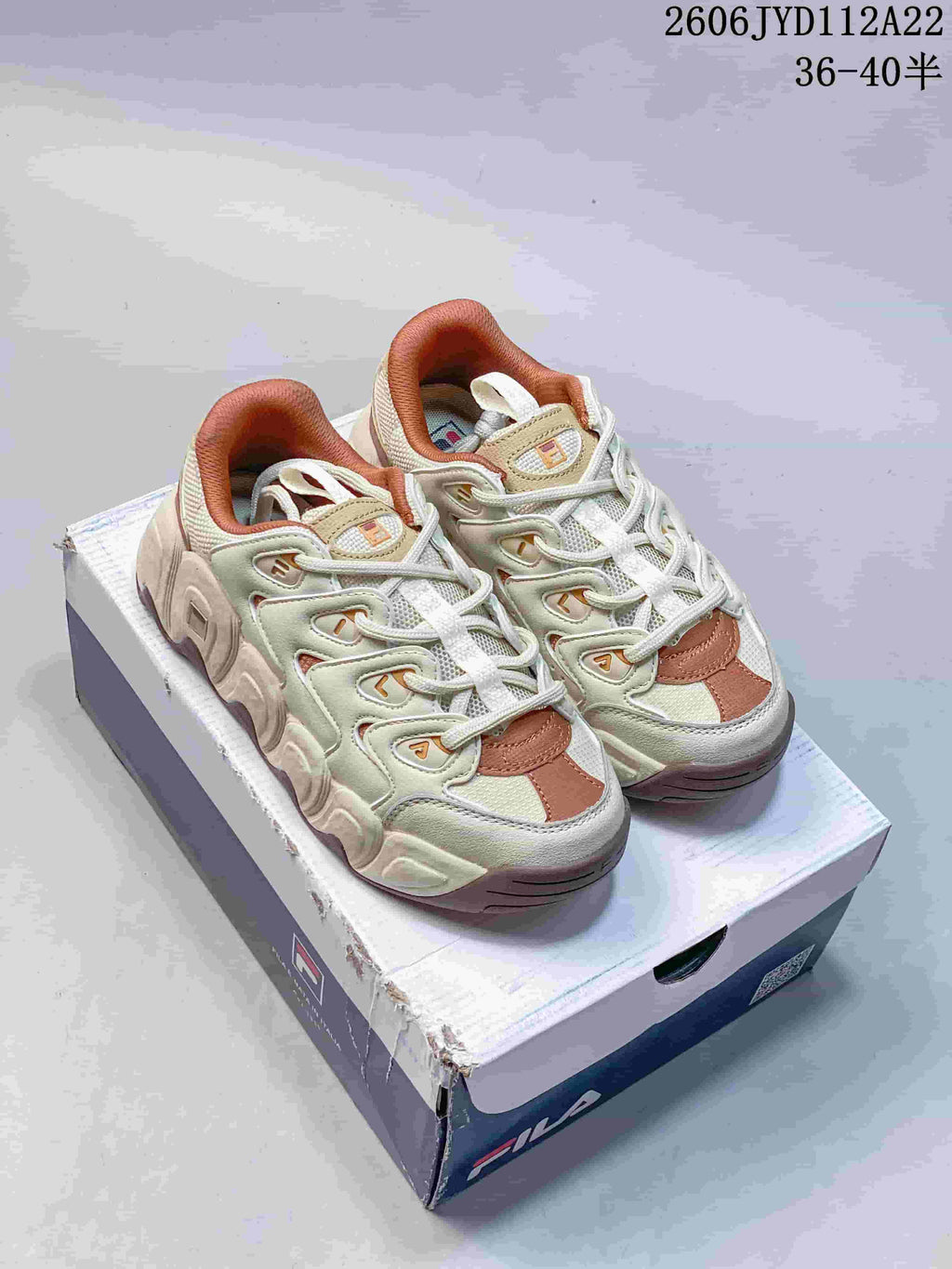 Pair of cream and rust FILA-style chunky sneakers shown on a shoebox