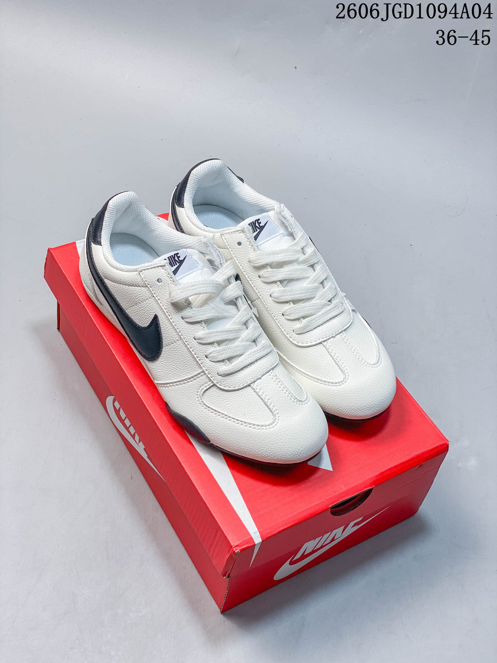 Pair of white Nike low-top sneakers with dark Swoosh accents, shown on a red shoe box