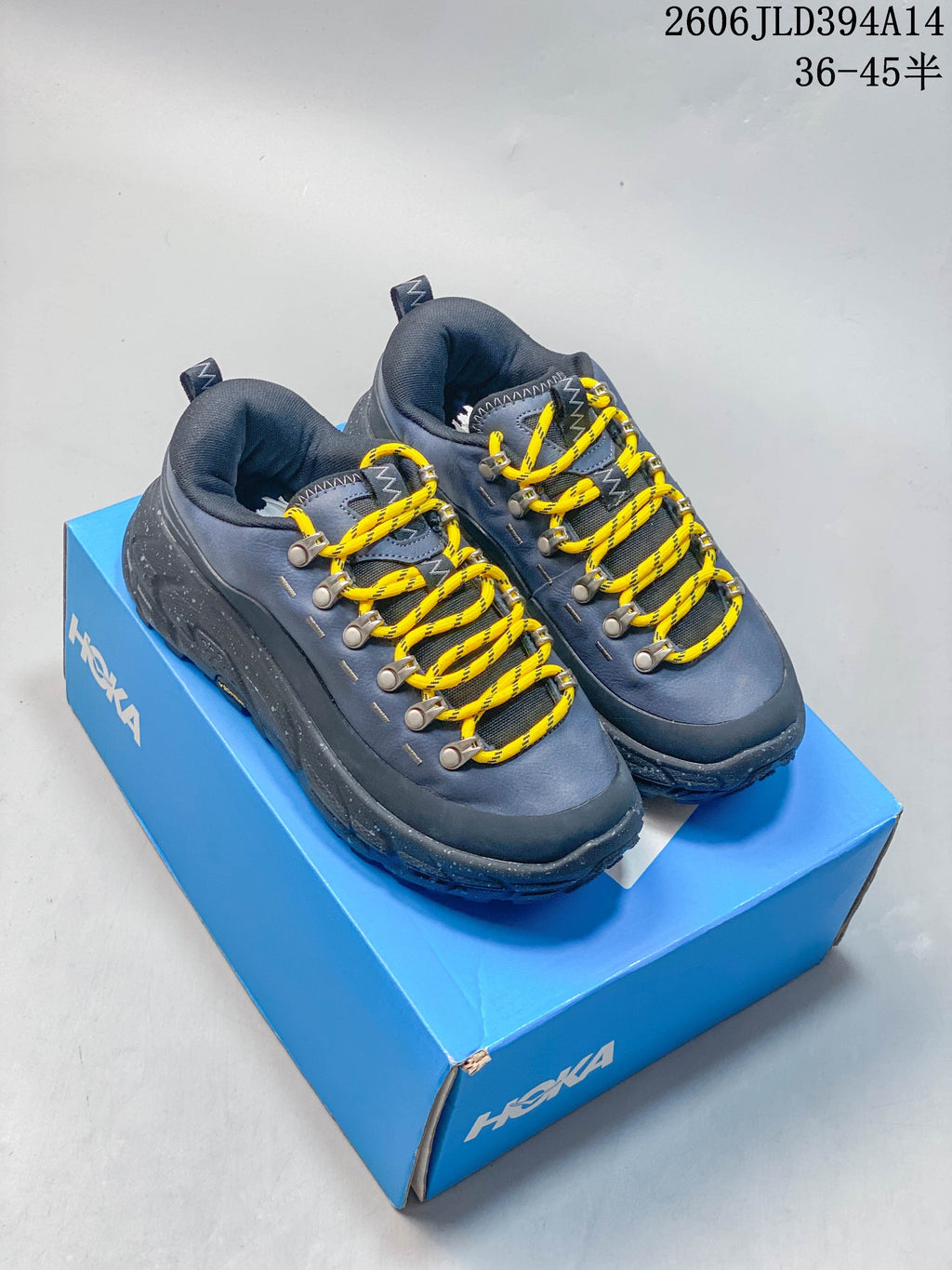 Pair of blue-gray HOKA low-top shoes with yellow laces on a blue shoe box.