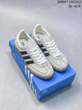 White Adidas Handball Spezial sneakers with navy stripes and gum-colored soles on a blue shoebox