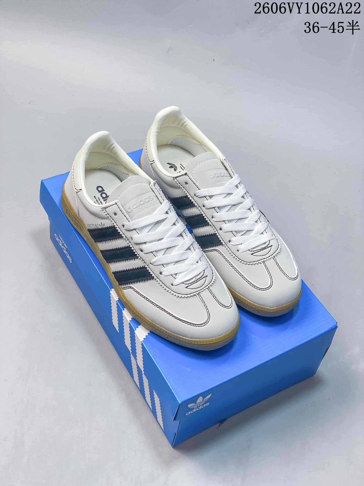 White Adidas Handball Spezial sneakers with navy stripes and gum-colored soles on a blue shoebox