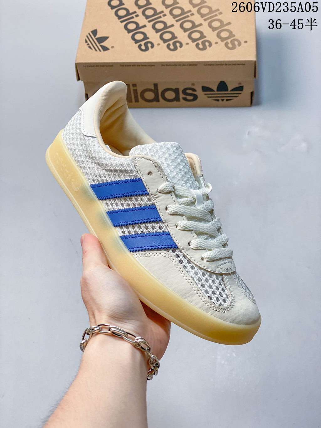 Angled side view of a white and light grey adidas Samba sneaker with blue stripes