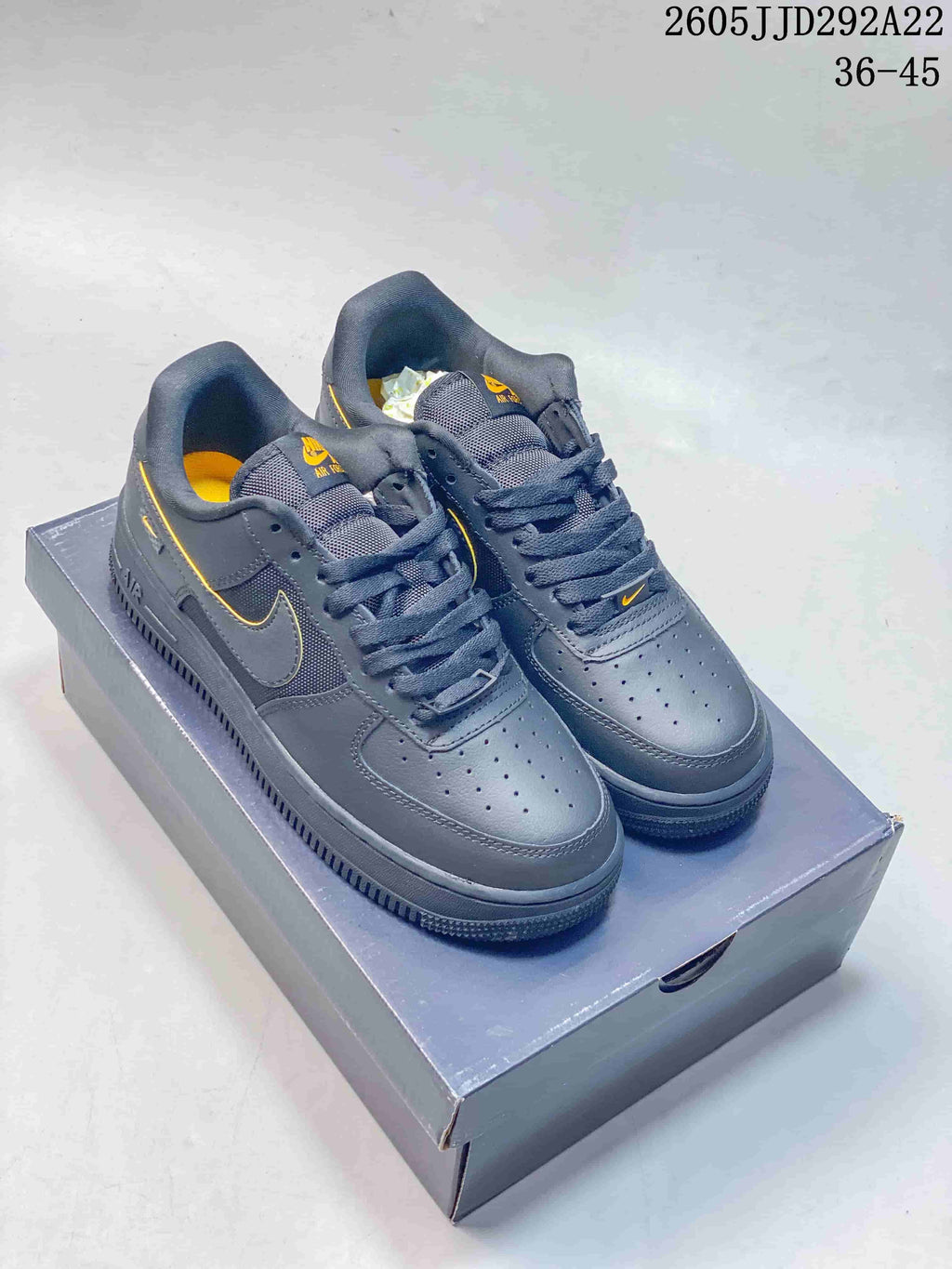 Pair of charcoal gray low-top sneakers with yellow accents, shown on a shoe box